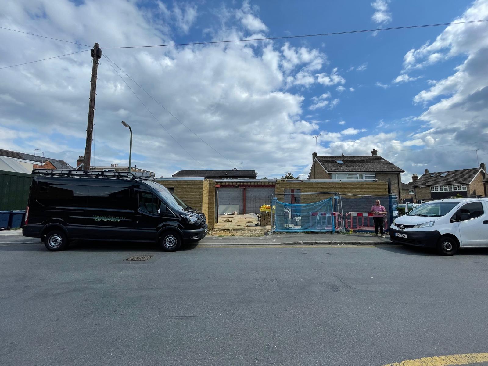 wide photo of van parked outside building without a roof
